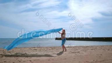 孕妇在风中飘着蓝色的布玩乐。 孕妇海滩